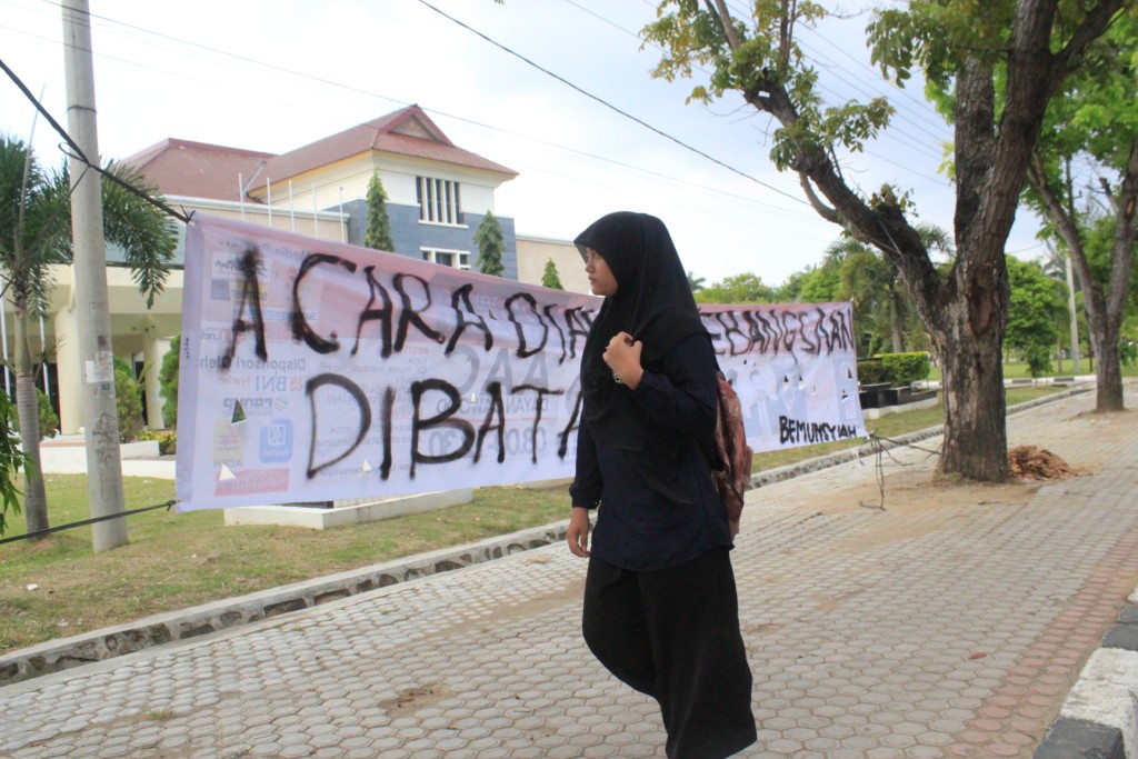 Foto 4 : Seorang wanita terlihat melewati spanduk yang bertuliskan “acara dialog kebangsaan dibatalkan” didepan gedung AAC. ( Tajul Ula-DETaK)